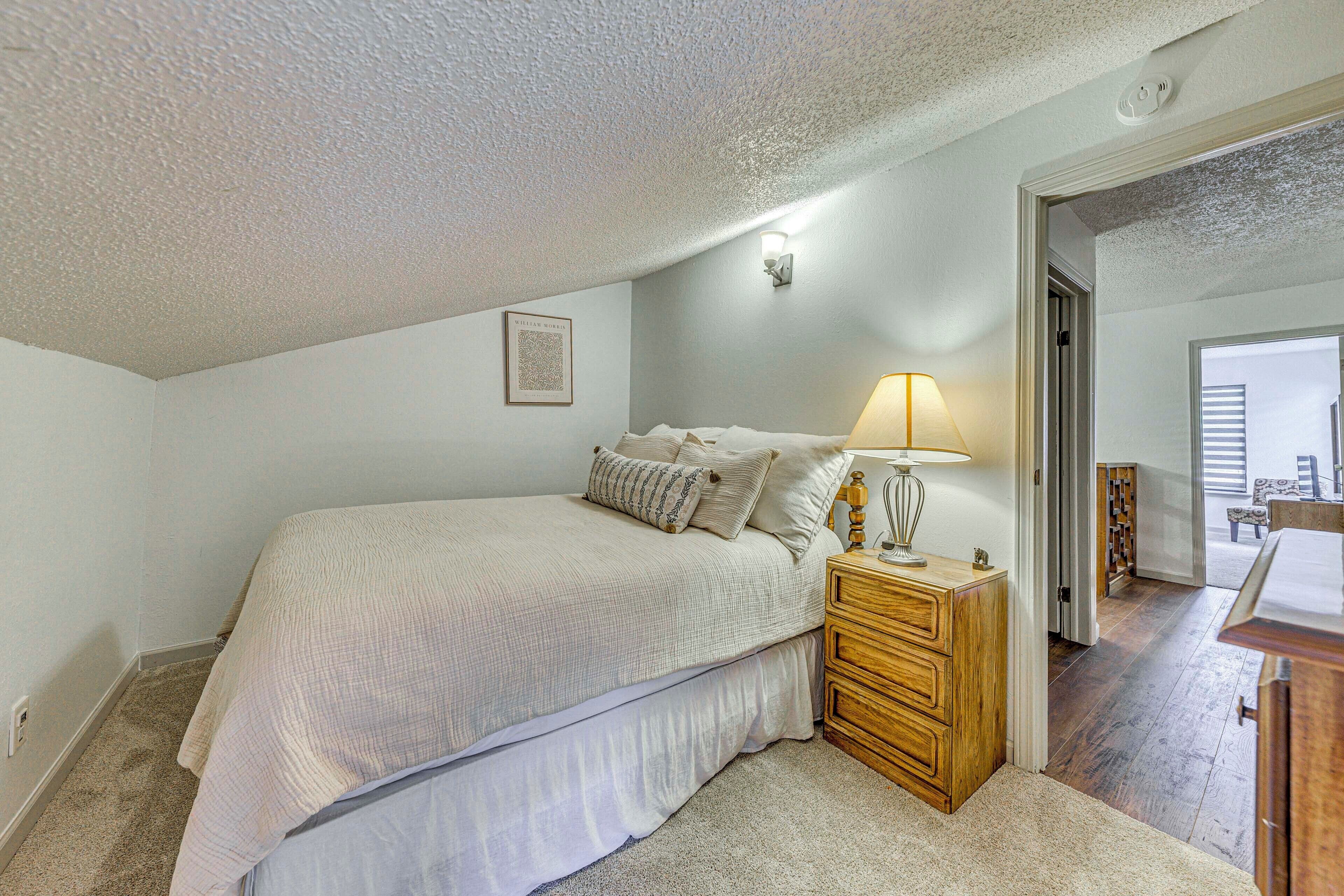 A bedroom with a bed, bedside table, lamp, and a door leading to another room.