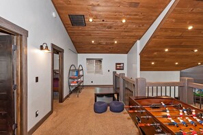 A room with a wooden ceiling, a foosball table, a bookshelf, and a window with blinds.