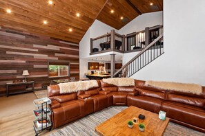 Una sala de estar moderna con un sofá seccional, una mesa de centro de madera y una escalera que conduce a un nivel superior.
