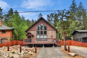 A two-story wooden cabin with a balcony, surrounded by a wooden fence and trees.