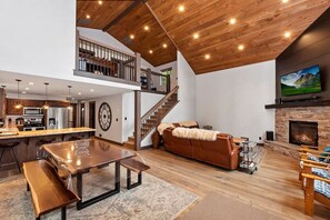 Un salón espacioso con techo de madera, chimenea, un reloj grande y televisor montado en la pared.