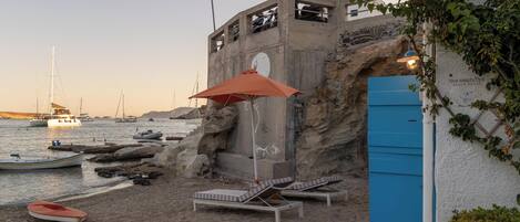 Un edificio frente a la playa con puerta azul, sillones de descanso y una sombrilla.