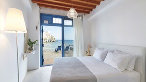 A bedroom with a bed, a lamp, a view of the beach, and a hanging light fixture. - The Elephant Goupa Beach (Kimolos)