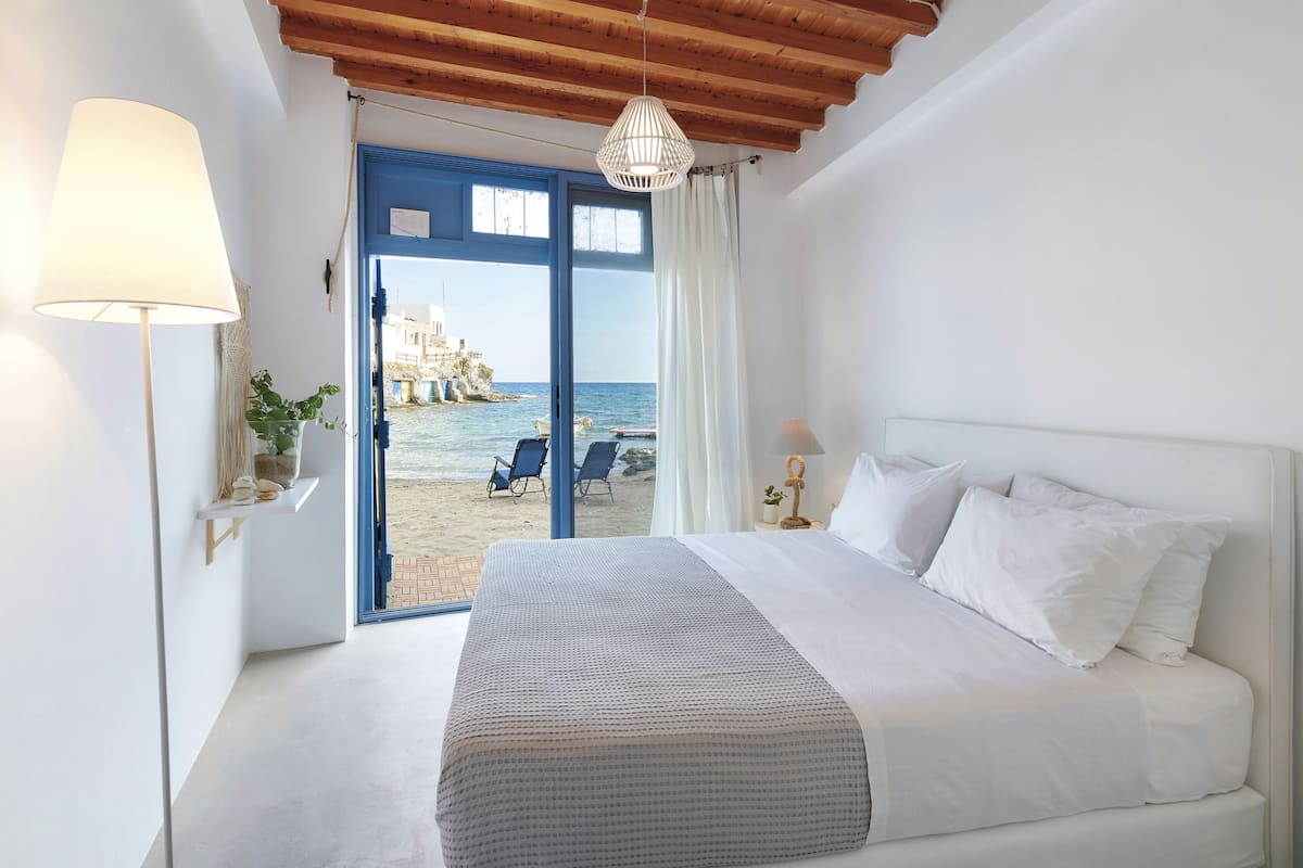 A bedroom with a bed, a lamp, a view of the beach, and a hanging light fixture.