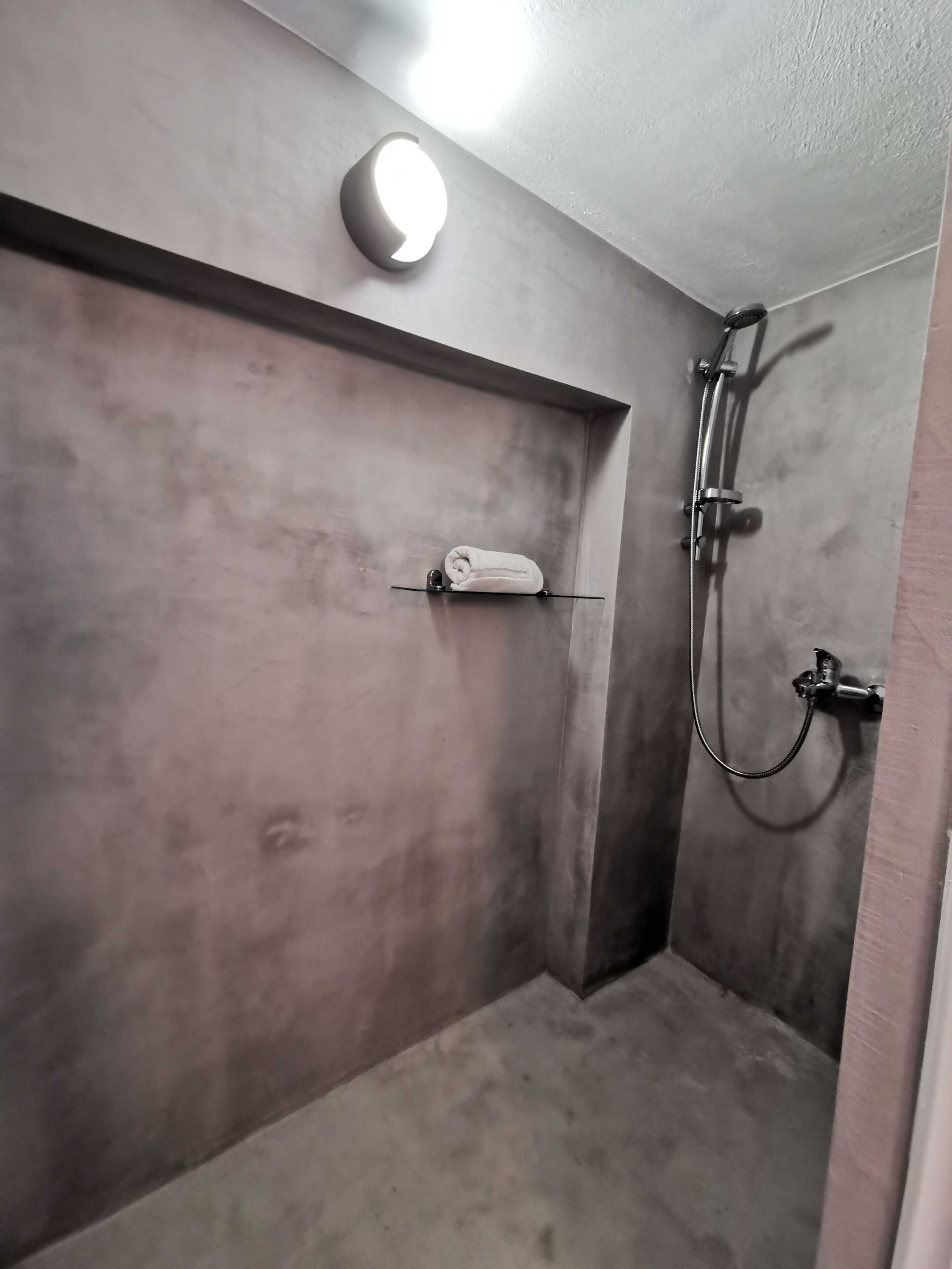 Un baño pequeño y poco iluminado con ducha, un perchero para toallas e iluminación en el techo.