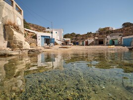Zona costera con agua cristalina, costa rocosa y edificios con puertas azules.
