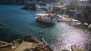 A coastal town with clear blue waters, boats docked at the harbor, and buildings with balconies overlooking the sea. - The Elephant Goupa Beach (Kimolos)