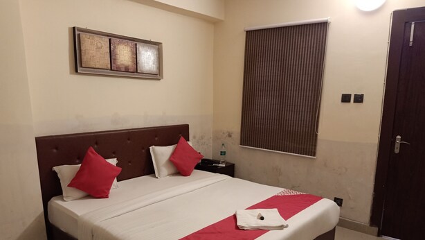 A neatly made bed with a red and white bedspread, a wooden headboard, and a single pillow. - Hotel Jaypee Inn (Howrah)