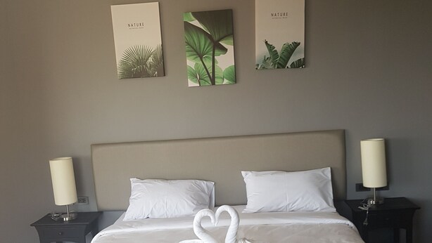 Un lit bien fait, avec des draps blancs et deux oreillers en forme de cygne, une tête de lit grise et trois tableaux encadrés sur le thème de la nature accrochés au mur.
