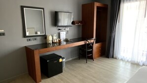 Une chambre d’hôtel moderne avec un bureau en bois, un téléviseur à écran plat fixé au mur, une armoire et un petit réfrigérateur noir.