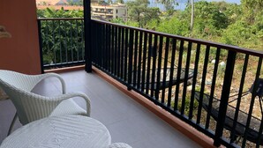 Un balcon avec des fauteuils en osier, une rambarde en métal noir et une vue sur des palmiers et des immeubles.