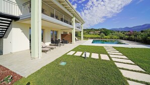 Una casa moderna de dos pisos con piscina, mobiliario exterior y vistas a las montañas.