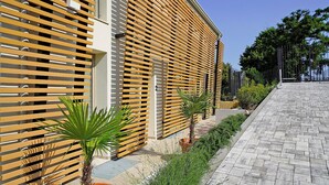 Un edificio moderno con listones horizontales de madera, un sendero pavimentado y plantas en macetas.