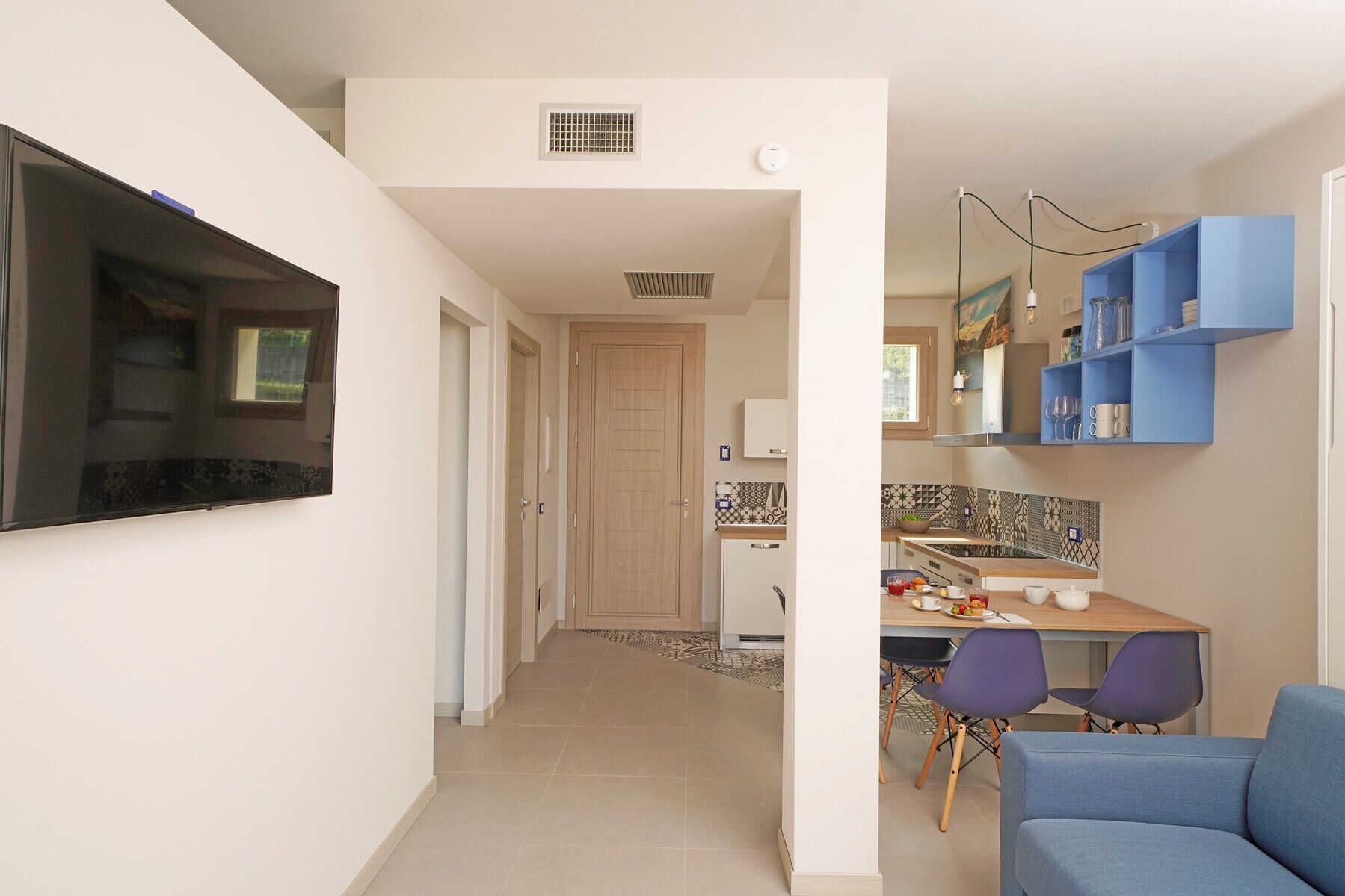 Een moderne keuken met een eethoek, een televisie aan de muur en een blauwe bank in de woonkamer.