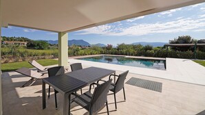 An outdoor pool area with a table and chairs, surrounded by a covered patio. - Gardaliva studio: in small residence with pool near to the lake (Manerba del Garda)