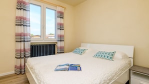 A neatly made bed with a white duvet and two patterned pillows, a bedside table with a lamp, and a window with striped curtains. - villa sole: with private pool near to the beach (Manerba del Garda)