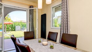 A dining area with a table set for four, a glass door leading to a garden, and a view of the outdoors. - villa sole: with private pool near to the beach (Manerba del Garda)