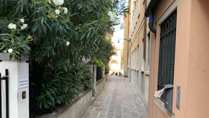 A narrow alleyway with a stone pavement, flanked by greenery and buildings. - Venice Sweet Home (Venice)