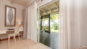 A room with a desk, chair, and a view of a deck with outdoor furniture. - Palm Beach Resort & Spa (Nosy Be)