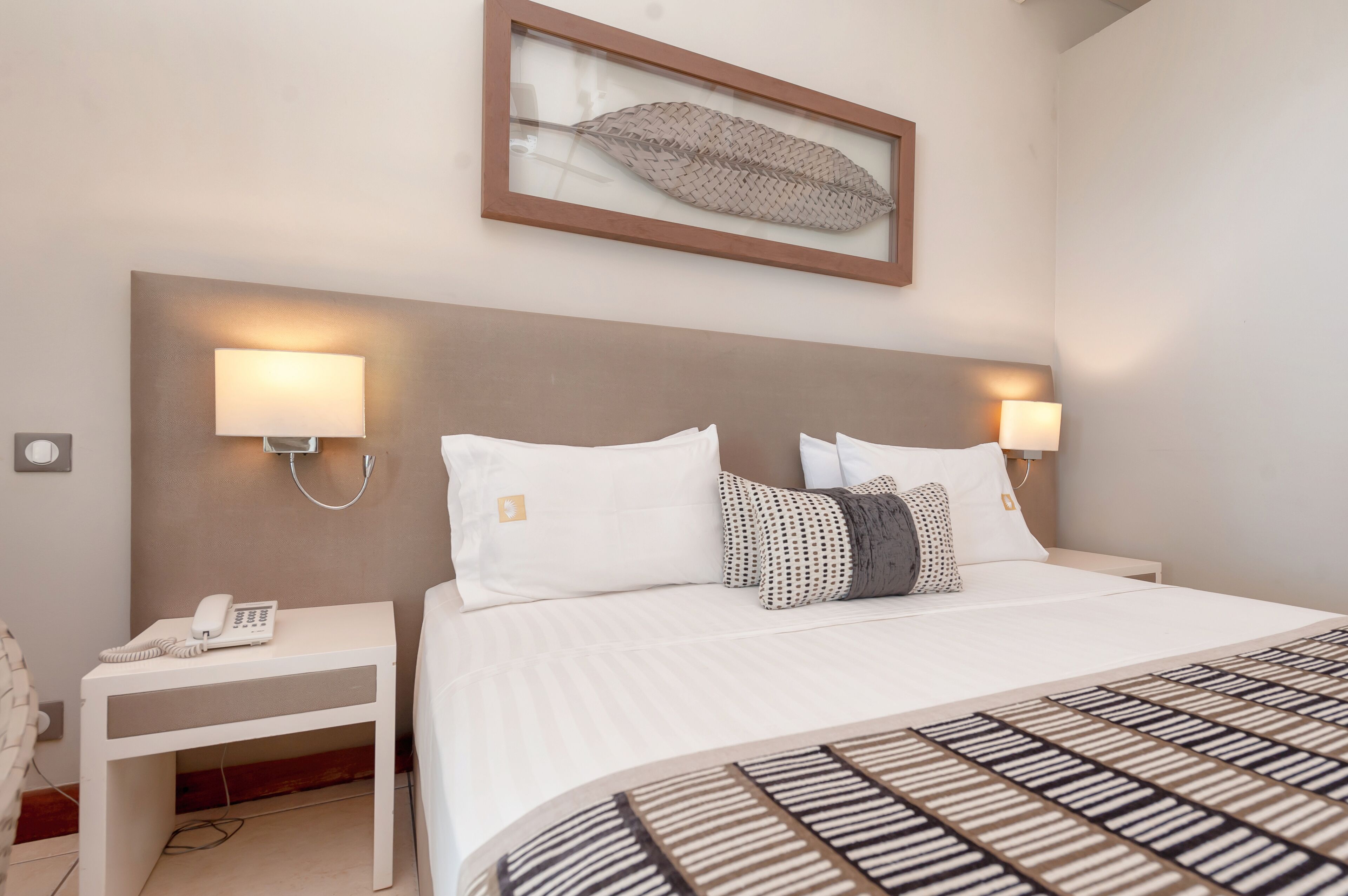 A hotel room with a large bed, two bedside tables with lamps, a framed artwork above the bed, and a telephone on one of the tables.