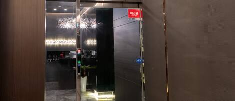 Pasillo interior que conduce a 'The Mains Bar' con una puerta de vidrio, una cámara de seguridad y un letrero que indica una zona para fumadores.