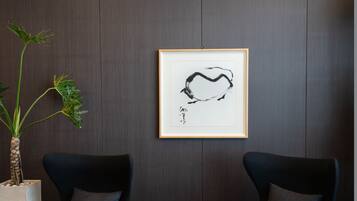 A room with two dark blue armchairs, a round wooden table, and a framed abstract artwork on the wall.