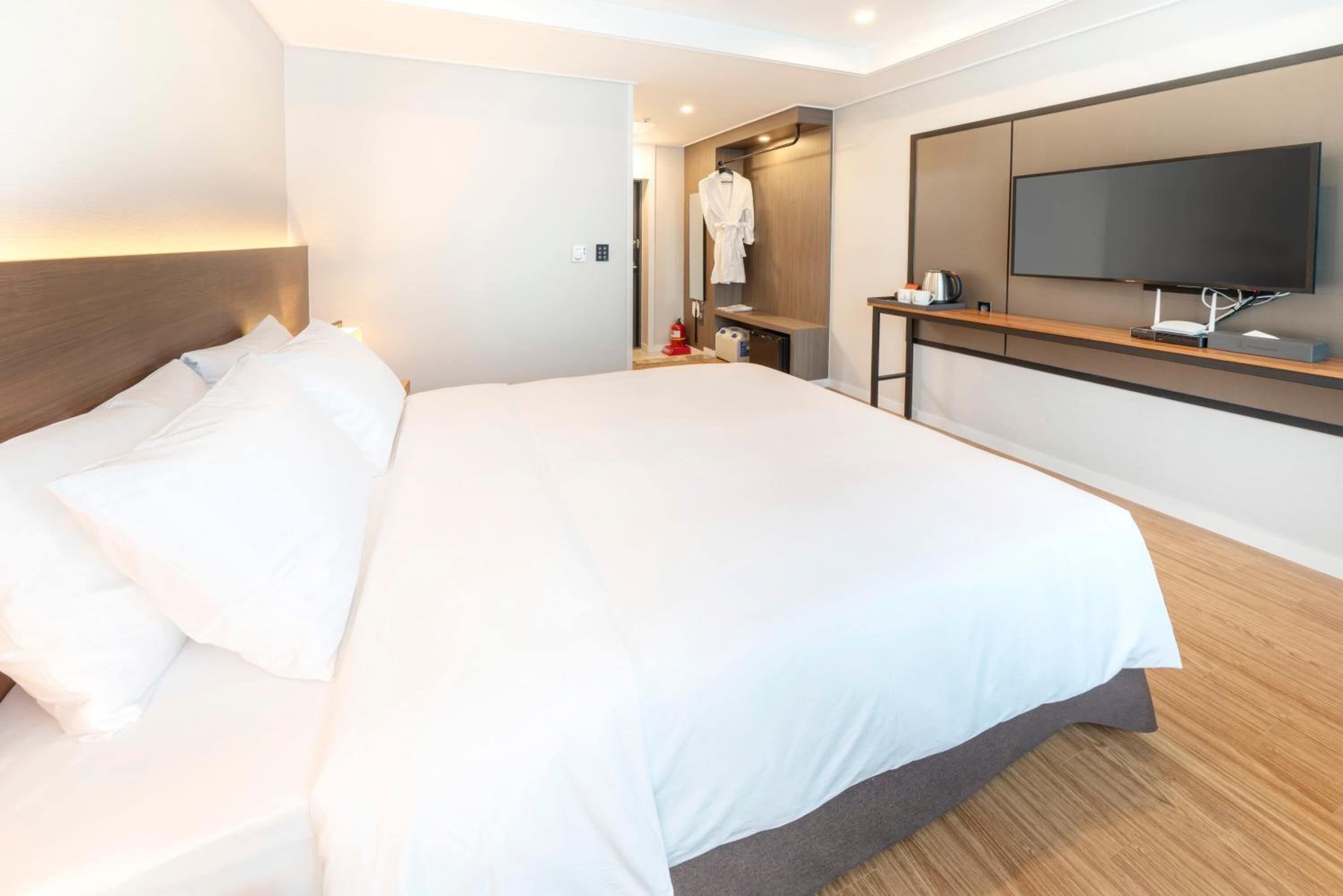 A hotel room with a large bed, a TV mounted on the wall, and a wooden bedside table.