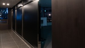 Corredor moderno com placa indicando uma sala de conferências, porta de vidro e vista da cidade à noite.