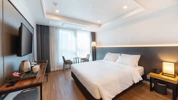 Ein modernes Hotelzimmer mit einem großen Bett, einem Schreibtisch mit einem Flachbildfernseher, einer Kaffeemaschine und einer kleinen Sitzecke mit Stühlen.
