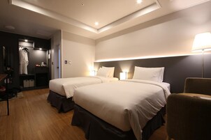Una habitación de hotel con dos camas, una silla, un escritorio y un armario.