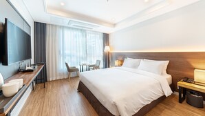 Quarto de hotel moderno com uma cama grande, televisão de tela plana, escrivaninha com luminária e uma pequena área de estar.