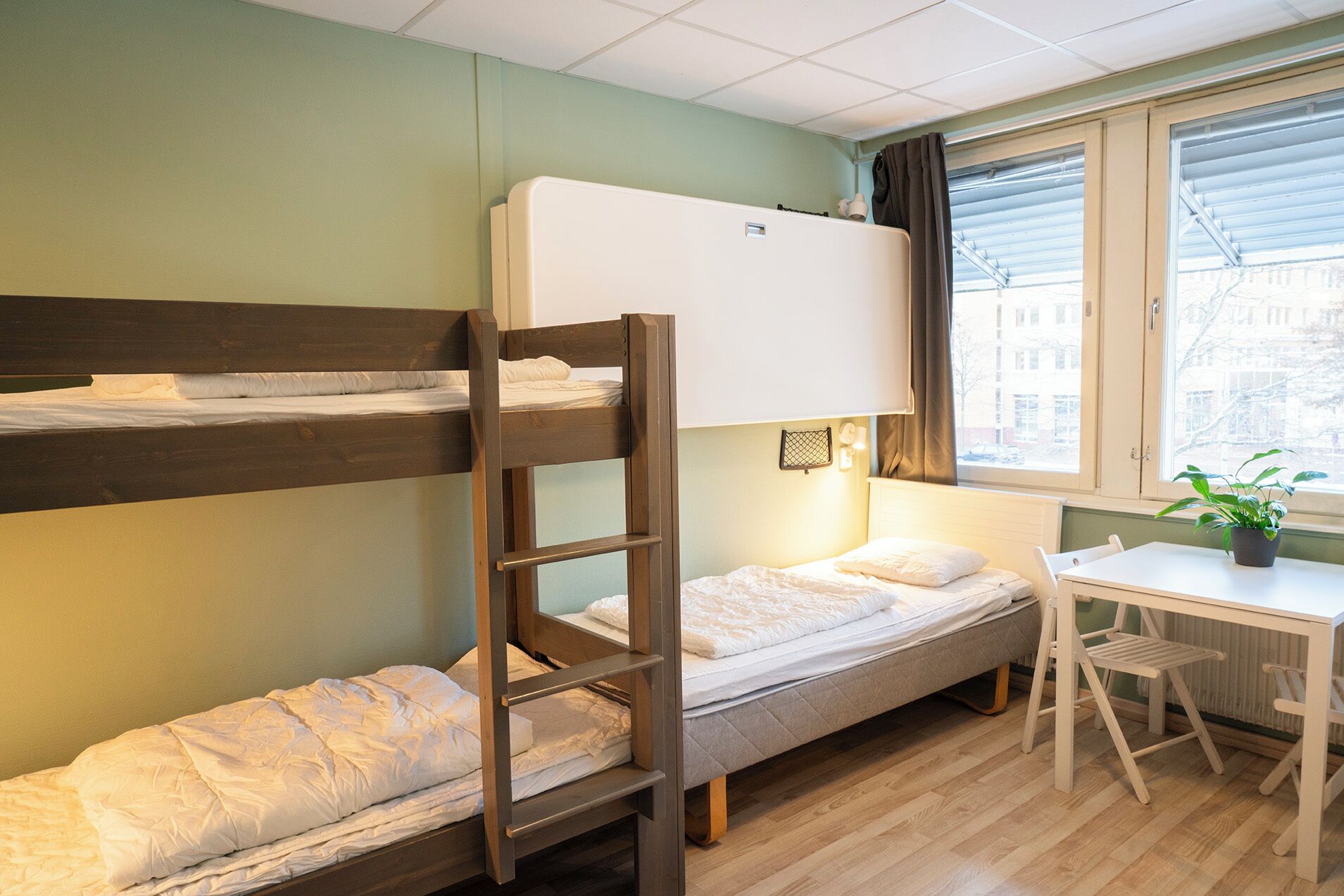 A dormitory room with bunk beds, a desk, and a window with a view of buildings.