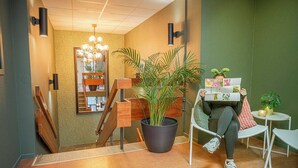 A modern interior with a staircase, a large potted plant, a reading area with a chair, and a small table with a plant. - Göteborg Hostel (Gothenburg)