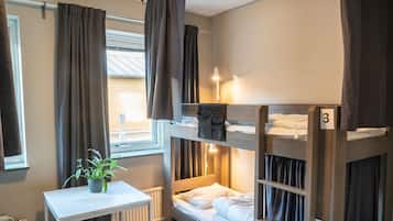 Un dormitorio con literas, una mesita con una planta y una ventana con cortinas.
