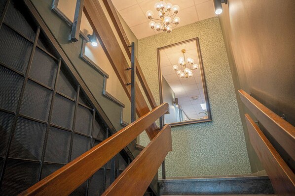 Una escalera con barandas de madera, pared texturizada y un candelabro.