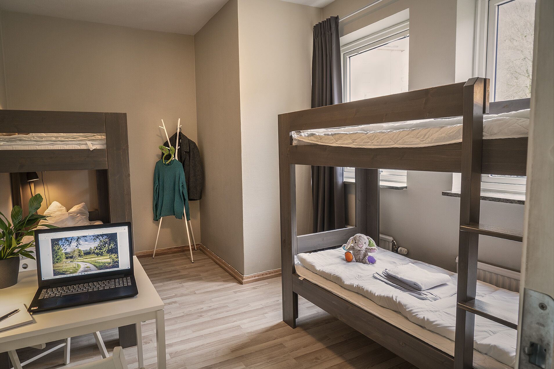 Una habitación con literas, un ordenador portátil sobre un escritorio y una planta.