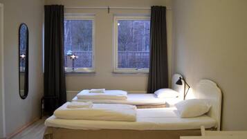 A bedroom with two beds, a bedside lamp, and a window with curtains.