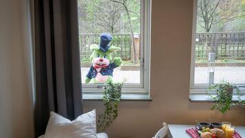 A room with a window, a radiator, a white chair, a table with breakfast items, and a plush toy outside the window.