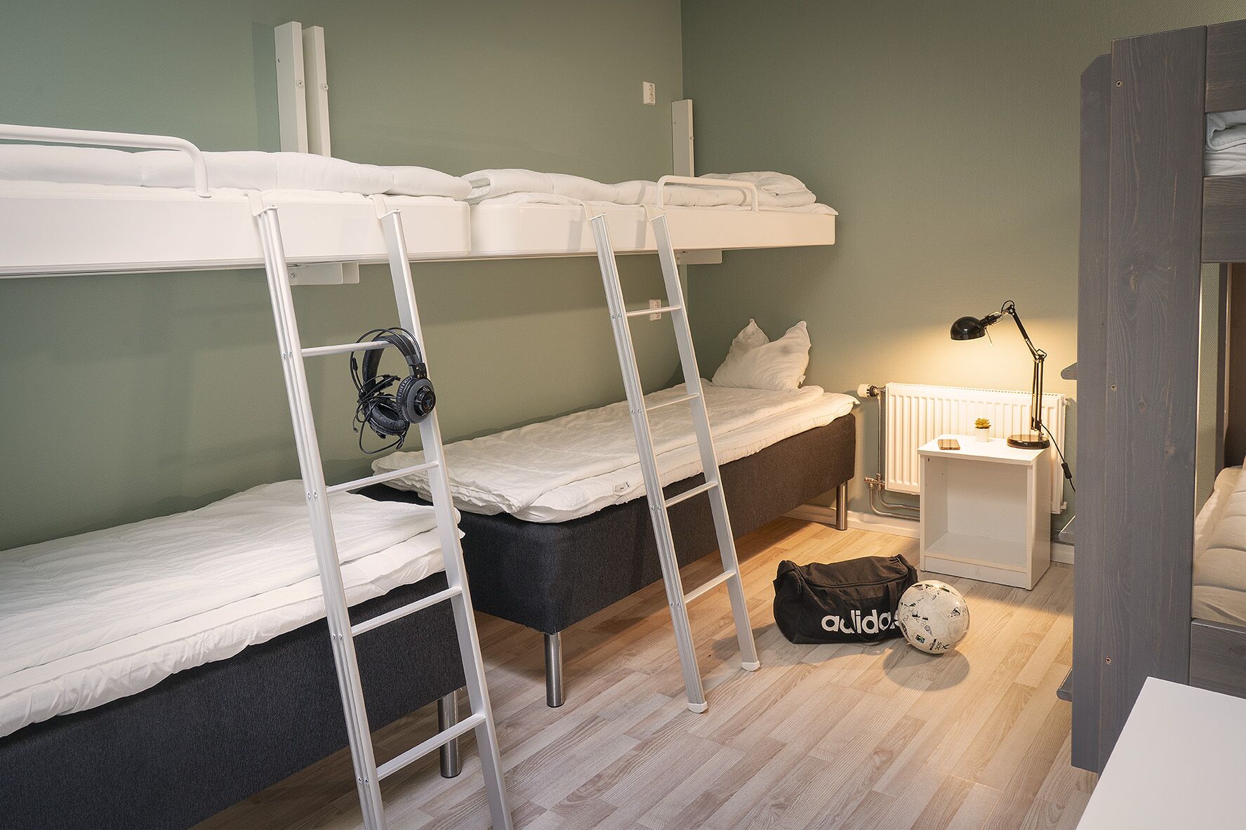 Una habitación tipo dormitorio con literas, un escritorio con lámpara y una mochila en el suelo.