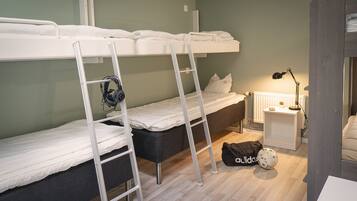 Una habitación tipo dormitorio con literas, un escritorio con lámpara y una mochila en el suelo.