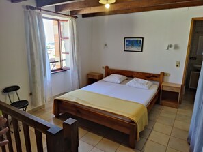 Un dormitorio con una cama de madera, dos mesitas de noche, un ventanal con cortinas, un escritorio pequeño y un cuadro en la pared.