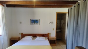 Un dormitorio con cama de madera, dos mesitas de noche, una mesita auxiliar, un cuadro en la pared y un baño visible a través de una puerta abierta.