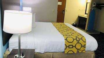 Una habitación de hotel con una cama, una lámpara de noche, una mesita con un teléfono y un baño al fondo.