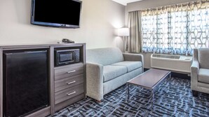 Ett hotellrum med en platt-TV, en soffa, ett soffbord och ett skrivbord med en lampa.