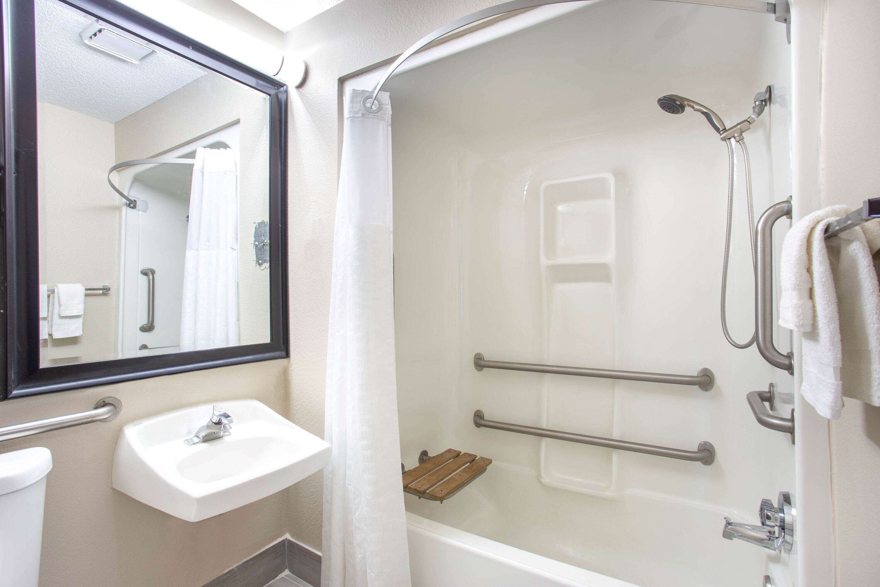 A bathroom with a sink, mirror, shower, and grab bars.