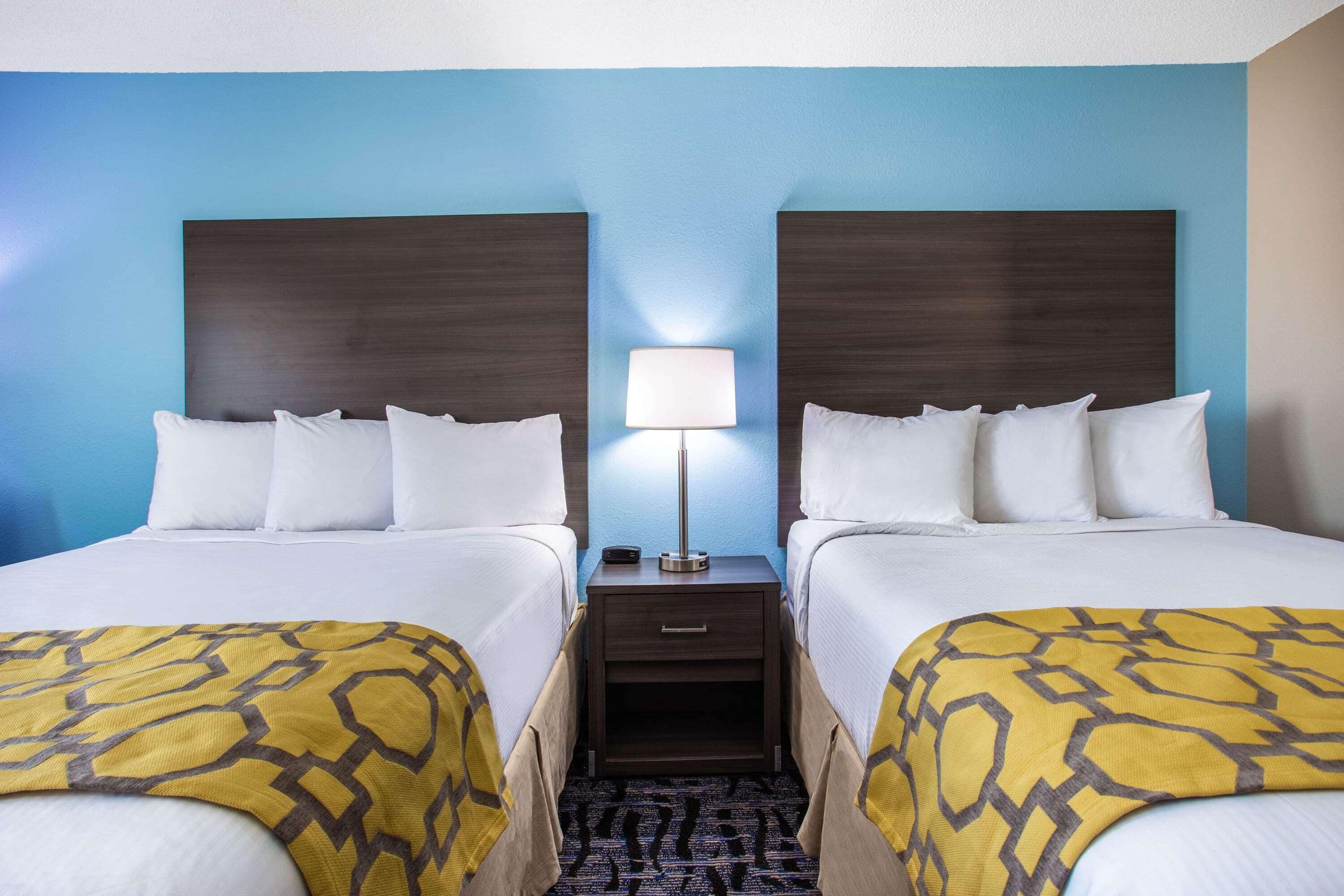 A hotel room with two beds, a nightstand with a lamp, and a patterned throw blanket.
