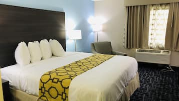 A hotel room with a large bed, two bedside lamps, a chair, an air conditioning unit, and a window with curtains.