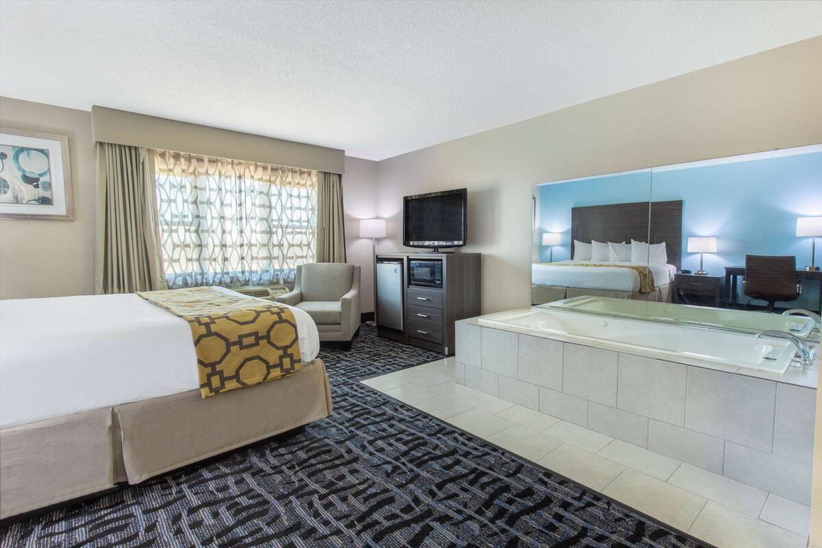Une chambre d’hôtel avec un lit, un bureau équipé d’un ordinateur, une télévision, un grand miroir et une baignoire.
