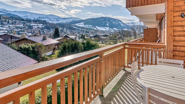 A wooden balcony with a view of a snow-covered mountain range and a town below. - Cozy apartment with mezzanine in Megève, near ski slopes (Megève)