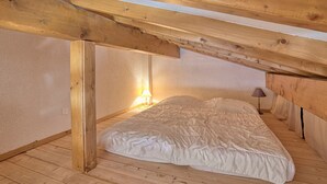 A bedroom with a sloped ceiling, wooden beams, a single bed with a white duvet, and a bedside lamp. - Cozy apartment with mezzanine in Megève, near ski slopes (Megève)